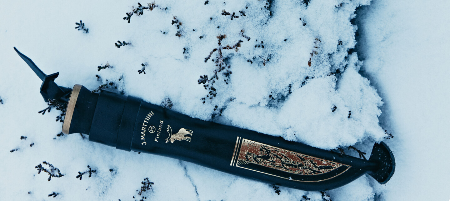 Handcrafted Marttiini knife with a polished wooden handle and engraved blade, resting on moss and autumn-colored forest ground.