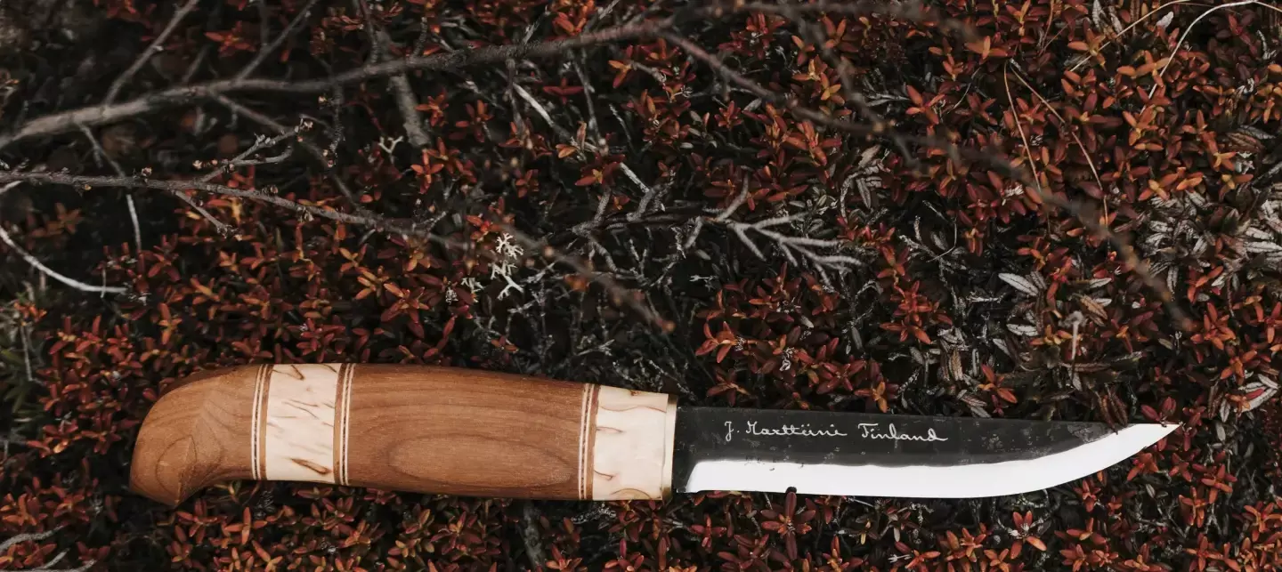 Couteau Marttiini artisanal avec manche en bois poli et lame gravée, posé sur de la mousse et des feuilles aux couleurs d’automne.