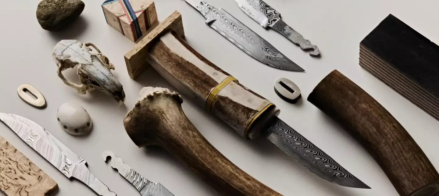 Erilaisia veitsenteriä, luukahvoja ja veitsen valmistusmateriaaleja valkoisella pöydällä.