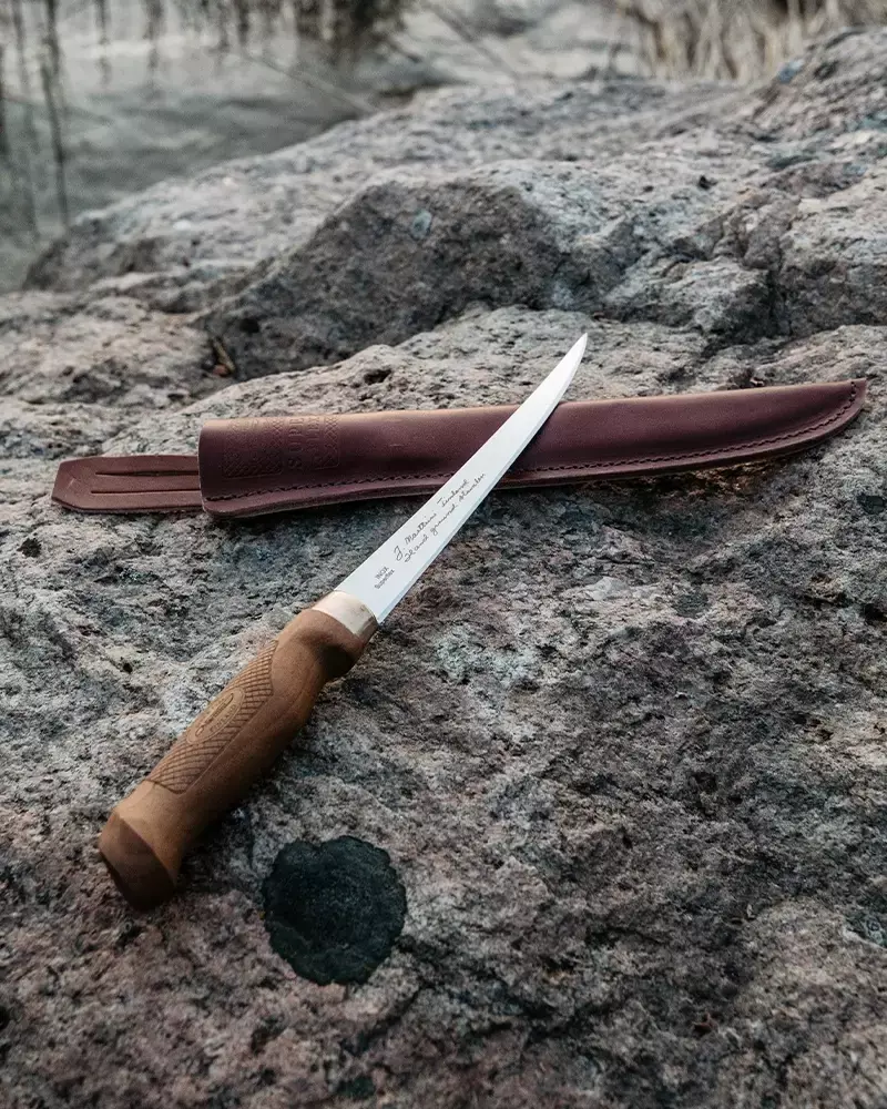 Marttiini Filetiermesser mit Holzgriff und brauner Scheide auf Felsen am See.