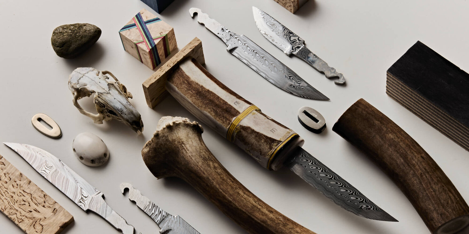 Various knife blades, bone handles, and knife-making materials on a white table.
